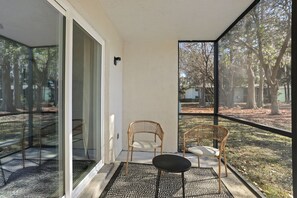 A balcony with a glass door, wicker chairs, a small table, and a view of trees and a yard.