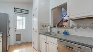 Una cocina con armarios blancos, un refrigerador de acero inoxidable, un lavavajillas y un ventanal con marco de metal decorativo.