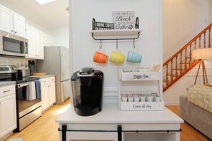 Een keuken met witte kasten, een koffiezetapparaat, kleurrijke mokken en een bord met daarop ‘koffiebar’.