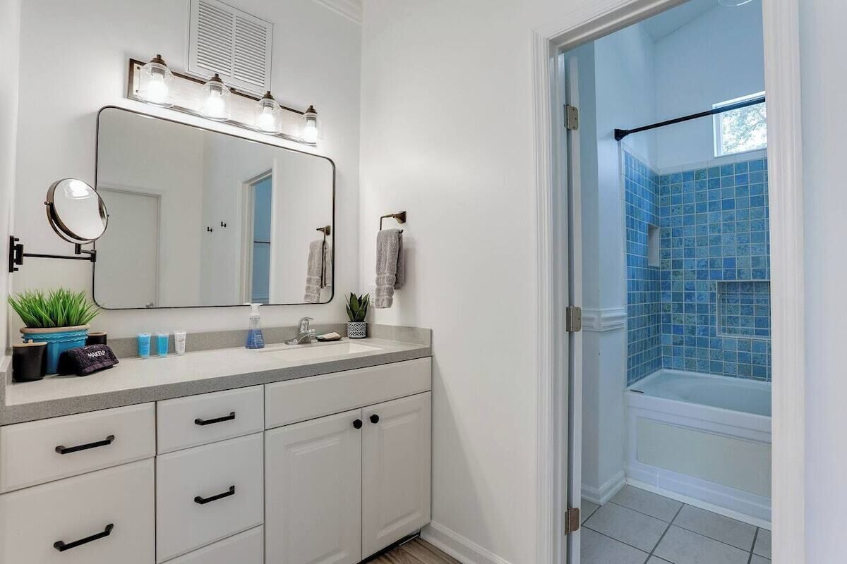 A bathroom with a large mirror, vanity with drawers, a sink, and a shower with blue tiles.