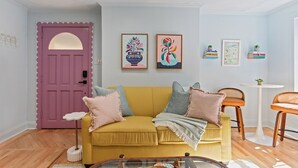 Ein Wohnzimmer mit einem gelben Sofa, einer rosafarbenen Tür und Wandbildern.