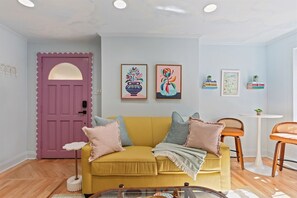 A living room with a yellow sofa, a pink door, and wall art. - Downtown Savannah * Fun Studio on Jones Street * Walk to Forsyth * Dogs OK (Savannah)
