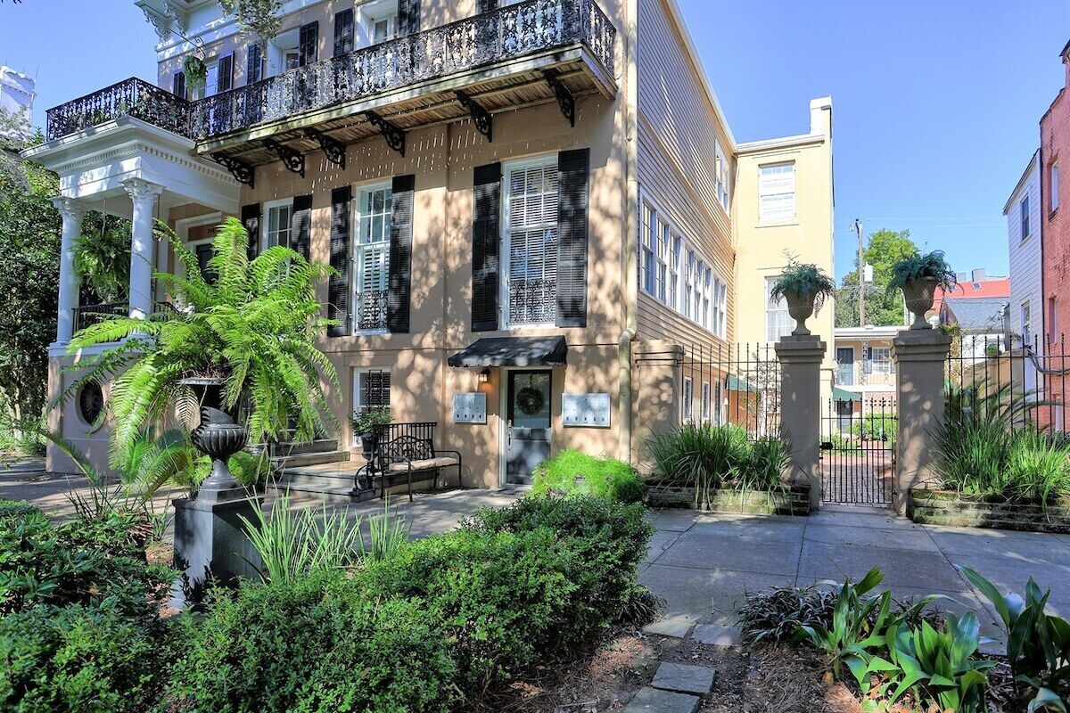 A two-story building with a balcony, a covered entrance, and a garden with a fountain.