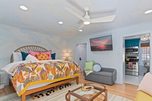 A bedroom with a bed, a ceiling fan, a bedside table, a lamp, a sofa, and a view into the kitchen. - Downtown Savannah * Fun Studio on Jones Street * Walk to Forsyth * Dogs OK (Savannah)