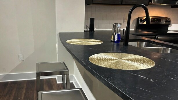 Et køkken med en sort marmorbordplade, to stålstole og en indbygget vask.