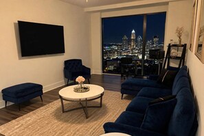 Ein modernes Wohnzimmer mit Stadtblick, einem Flachbildfernseher, einem runden Couchtisch und blauen Sofas.