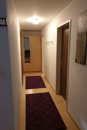 A hallway with wooden flooring, a door with a keyhole, a wall-mounted light fixture, and a piece of abstract art. - Curtinfess Franklin Appartement/Fewo, Bad, WC, 2 Schlafräume by Interhome (Bivio)