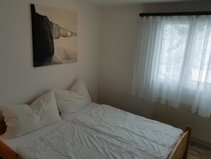 A bedroom with a bed, pillows, a painting, and a window with sheer curtains.