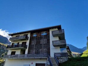 A multi-story building with balconies, a sign reading 'CARTINFESS,' and a mountainous backdrop.