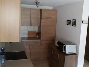 A compact kitchen with wooden cabinets, a microwave, and a small countertop. - Curtinfess Franklin Appartement/Fewo, Bad, WC, 2 Schlafräume by Interhome (Bivio)