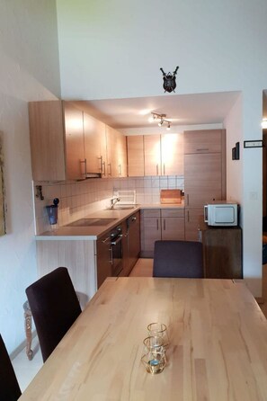 A compact kitchen with wooden cabinets, a microwave, and a dining table with chairs.