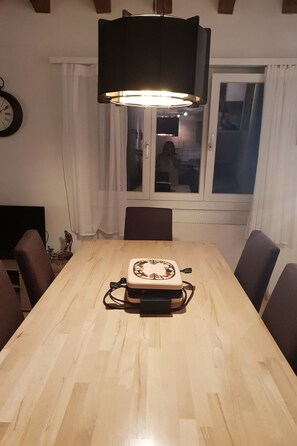 A dining table with a central appliance, surrounded by chairs, in a room with a window and curtains.