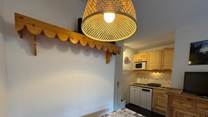 Une chambre à coucher comprenant un lit, une tête de lit en bois, une étagère fixée au mur, et un coin cuisine avec des placards, un four à micro-ondes et un téléviseur.
