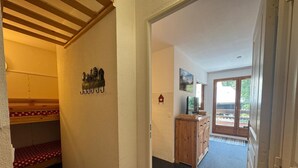 Un couloir avec un lit superposé, des armoires en bois, un téléviseur et une porte donnant sur un balcon.
