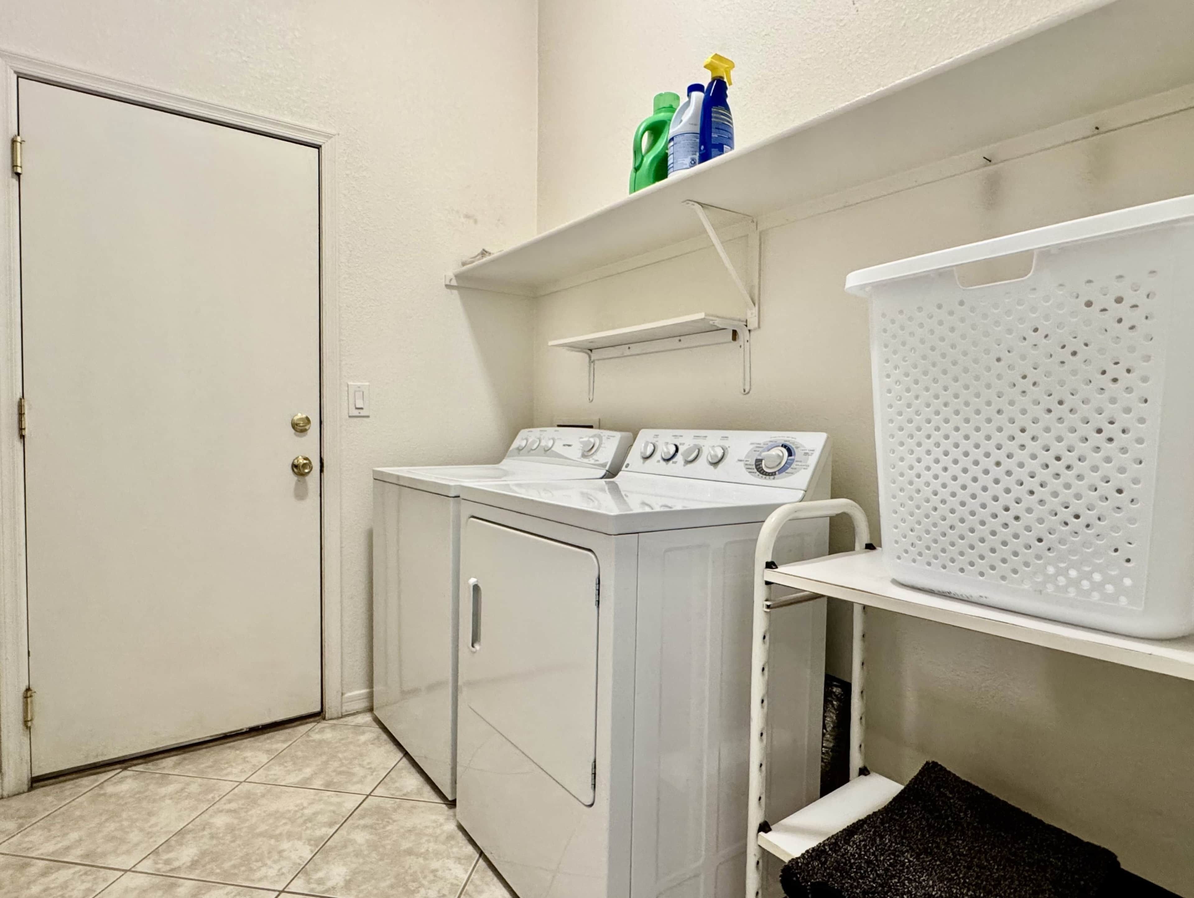 A laundry room with a washer and dryer, a shelf with cleaning supplies, and a basket.