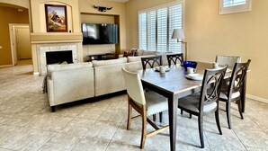 A living room with a fireplace, a television, and a dining area with a table and chairs. - Oro Valley Home For Rent w/ Spa & Views (Oro Valley)