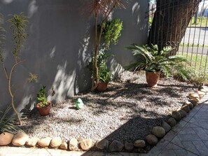 Un espace jardin aménagé avec des plantes en pot, un sol recouvert de gravier et une clôture en métal.