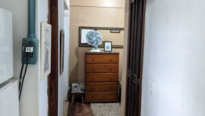 A narrow hallway with a wooden floor, a blue electrical outlet, a small stool, a wooden dresser, and a ceiling fan. - Studio Apartment Train at the Botanical Garden (Curitiba)