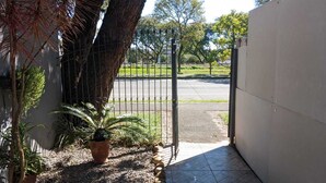 A gated entrance with a paved path leading to a road, surrounded by trees and potted plants. - Studio Apartment Train at the Botanical Garden (Curitiba)