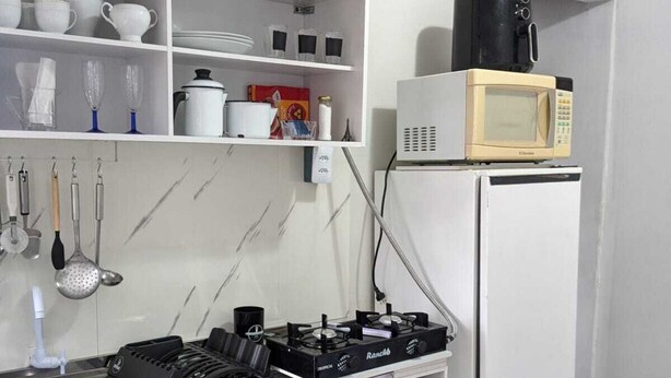 A compact kitchen with a gas stove, a microwave, and a sink. - Studio Apartment Train at the Botanical Garden (Curitiba)