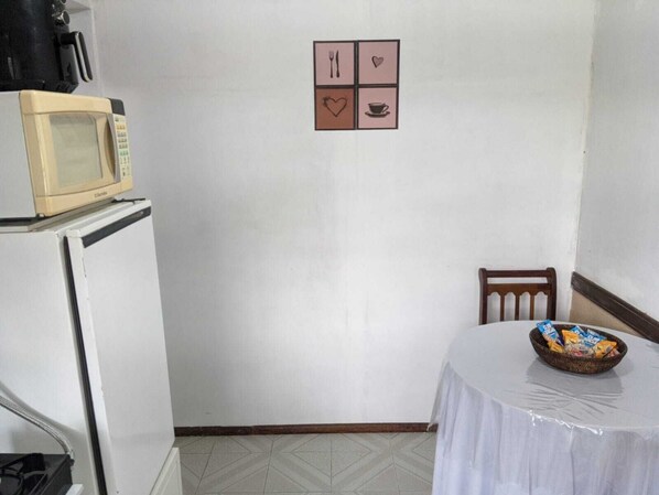 Une petite pièce avec un four à micro-ondes posé sur un meuble blanc, une table recouverte d’une nappe blanche et, au mur, un tableau représentant un cœur et une tasse.