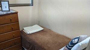 A small, single-bed room with a brown bedspread, a wooden dresser with drawers, and a framed certificate on top. - Studio Apartment Train at the Botanical Garden (Curitiba)