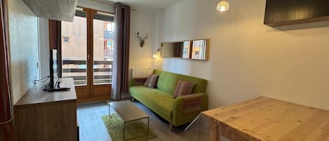 A compact living space with a green sofa, a wooden dining table, and a small coffee table.