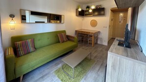 En kompakt opholdsstue med en grøn sofa, et lille spisebord og et fjernsyn på et træskab.