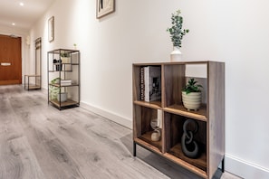 A hallway with a wooden floor, a metal-framed shelving unit with books and decorative items, and a potted plant. - Stylish Canal views Sleeps 8 | City Leeds Location (Leeds)
