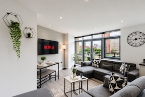 A modern living room with a sofa, coffee table, and a TV displaying 'NETFLIX'. - Stylish Canal views Sleeps 8 | City Leeds Location (Leeds)