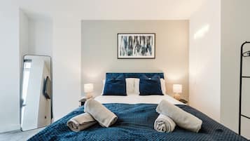 A modern hotel room with a bed, two bedside lamps, a large mirror, and a framed abstract painting on the wall.