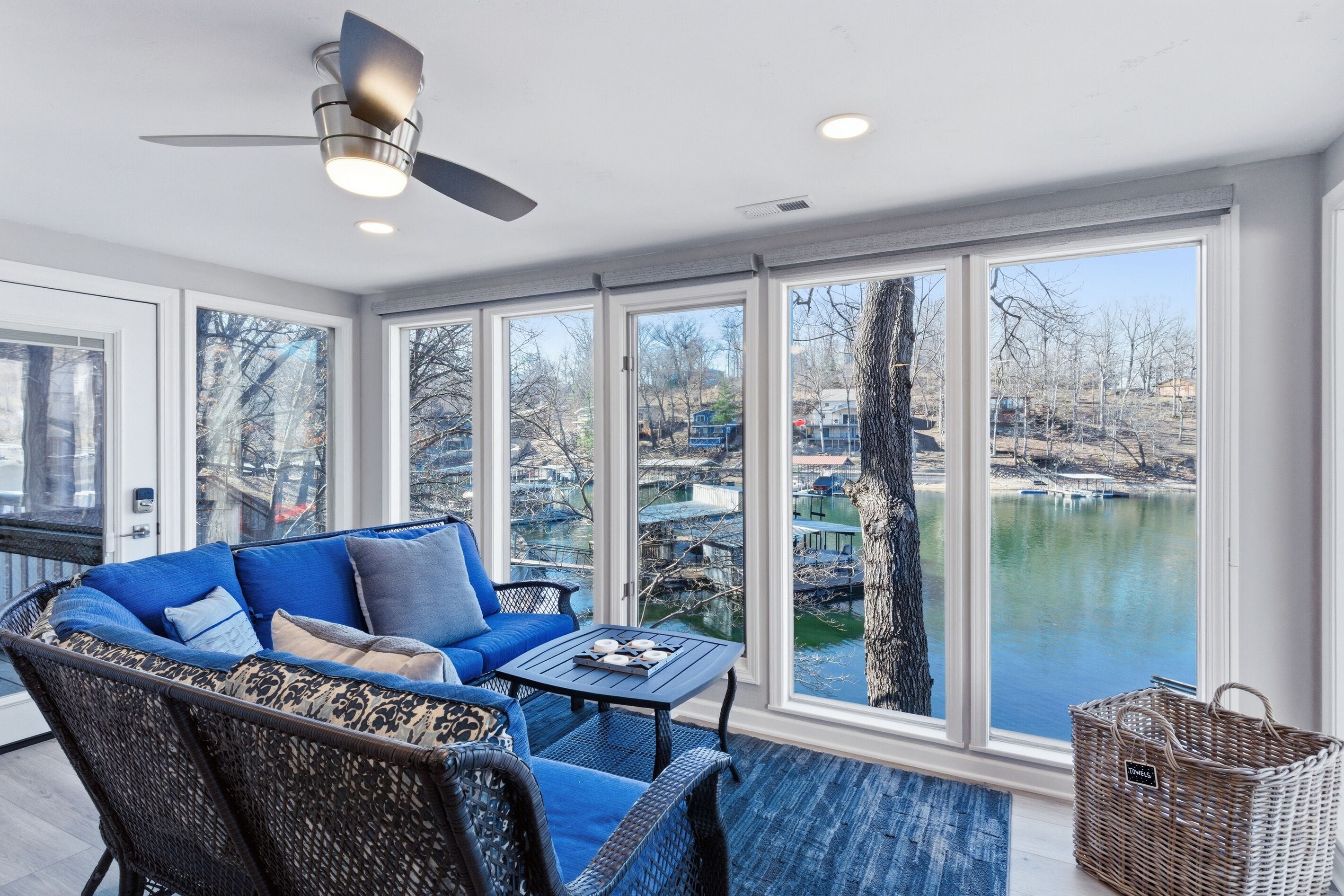 Une véranda avec vue sur un lac, un canapé bleu et un ventilateur de plafond.