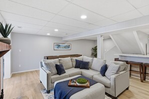 Ein modernes Wohnzimmer mit einem Ecksofa, einem Couchtisch mit Pflanze und einem Essbereich mit weißem Tisch und Stühlen.