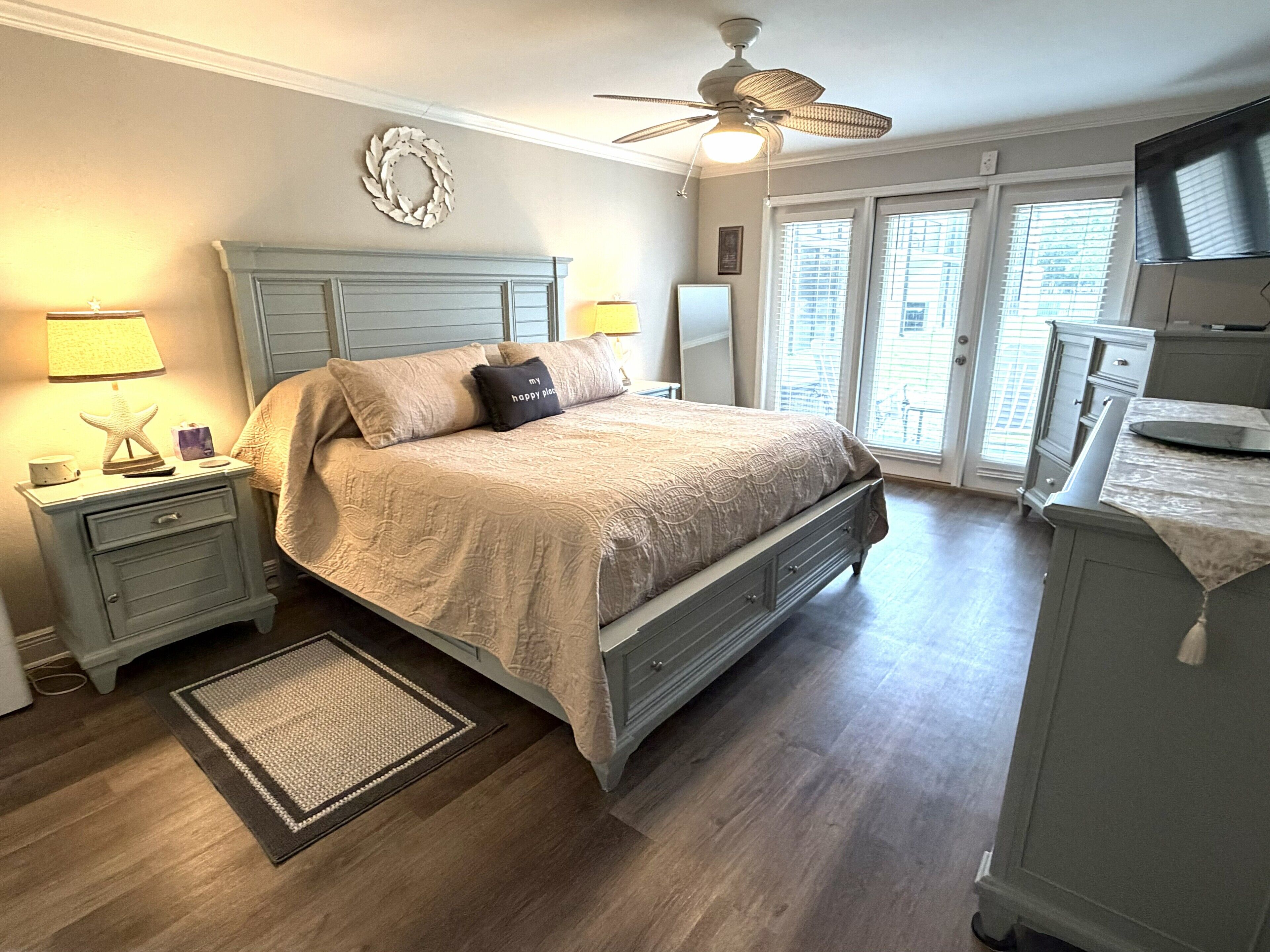 A bedroom with a bed, nightstands, a ceiling fan, a dresser, and a view through the door.