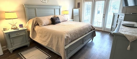 Ein Schlafzimmer mit Bett, Nachttischen, Deckenventilator, Kommode und Blick durch die Tür.