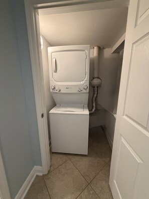 A compact laundry room with a washer and dryer, a small window, and a door leading to another room. - Biloxi Belle (Biloxi)