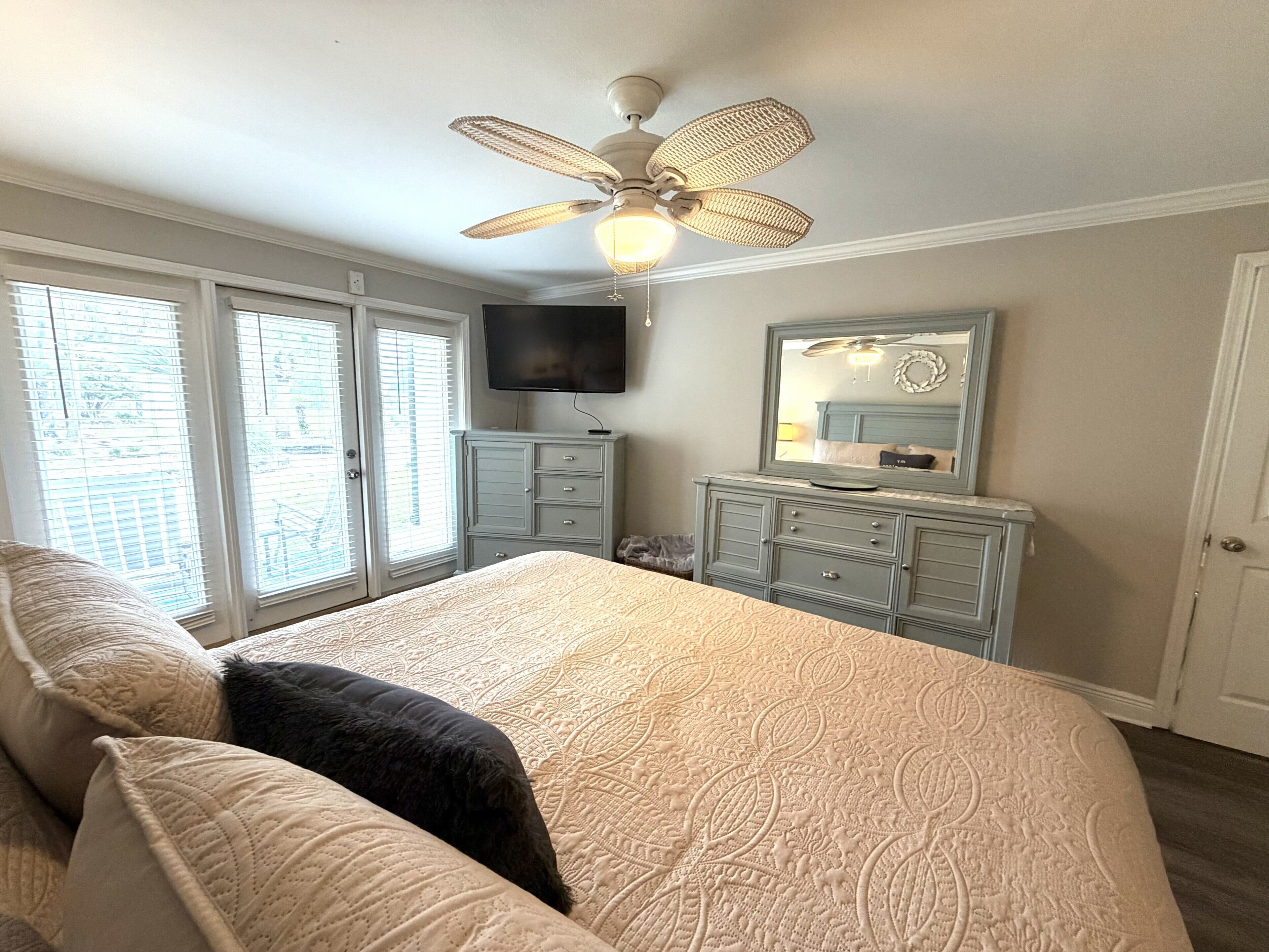 A bedroom with a bed, dresser, television, and a ceiling fan.