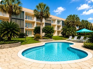 A pool area with a curved edge, surrounded by a stone patio. There are lounge chairs and a blue umbrella. - Biloxi Belle (Biloxi)