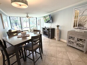 A dining area with a wooden table and chairs, a television mounted on the wall, and a fireplace. - Biloxi Belle (Biloxi)