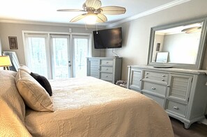 Quarto com cama, cômoda, televisão e ventoinha no teto.