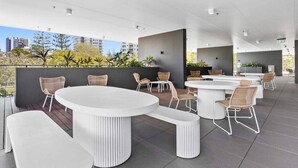 An outdoor seating area with round tables and wicker chairs, surrounded by a low wall and plants. - Luxury Penthouse | Sandbar Burleigh Heads (Gold Coast)