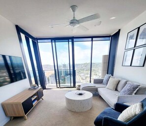 Ein modernes Wohnzimmer mit großem Fenster, Deckenventilator, Sofa, Couchtisch und Fernseher.