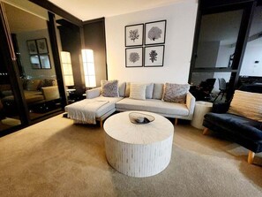 A modern living room with a sectional sofa, a round coffee table, and a large window. - Luxury Penthouse | Sandbar Burleigh Heads (Gold Coast)