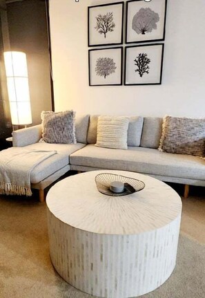 A living room with a sectional sofa, a round coffee table, and framed artwork on the wall. - Luxury Penthouse | Sandbar Burleigh Heads (Gold Coast)