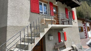 Un bâtiment à deux étages avec une façade en pierre, des volets rouges et un balcon doté de rampes en métal.
