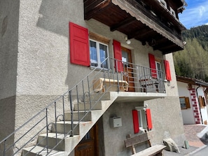 Ein zweistöckiges Gebäude mit Sandsteinfassade, roten Fensterläden und einem Balkon mit Metallgeländern.