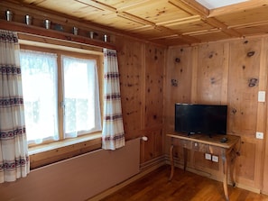 A wooden-paneled room with a window, curtains, a television on a wooden stand, and a radiator. - Tga Crap Appartement/Fewo, Dusche, WC, 1 Schlafraum 2.5 Zimmerwohnung - 4 Betten by Interhome (Savognin)