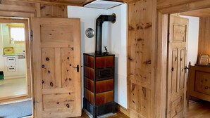 Un intérieur en bois avec une cheminée centrale, des portes en bois et un espace cuisine visible.