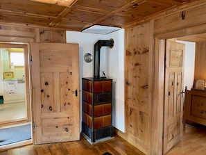 Ein Holzinnenraum mit Kamin im Zentrum, Holztüren und einem sichtbaren Küchenbereich.