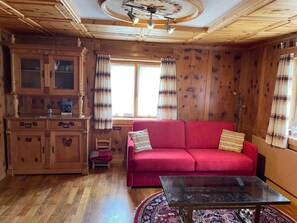 A wooden interior with a red sofa, a glass coffee table, and a wooden cabinet. - Tga Crap Appartement/Fewo, Dusche, WC, 1 Schlafraum 2.5 Zimmerwohnung - 4 Betten by Interhome (Savognin)